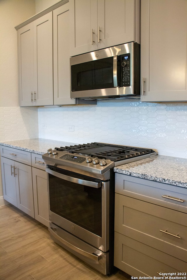 kitchen featuring backsplash, appliances with stainless steel finishes, gray cabinets, and light wood finished floors