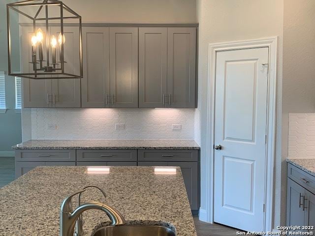 kitchen with light stone countertops, a sink, gray cabinetry, decorative light fixtures, and backsplash