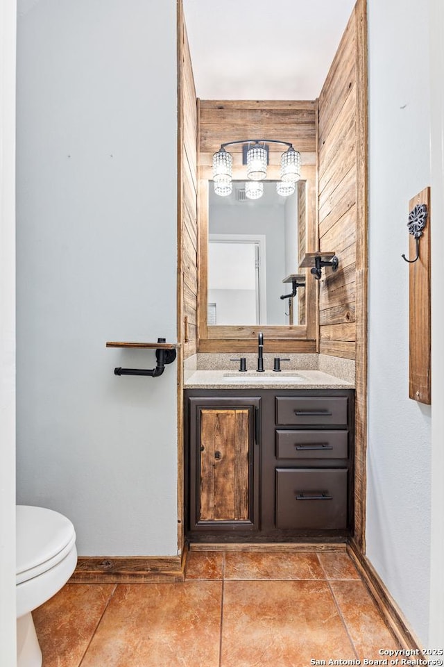 half bath with tile patterned floors, baseboards, toilet, and vanity