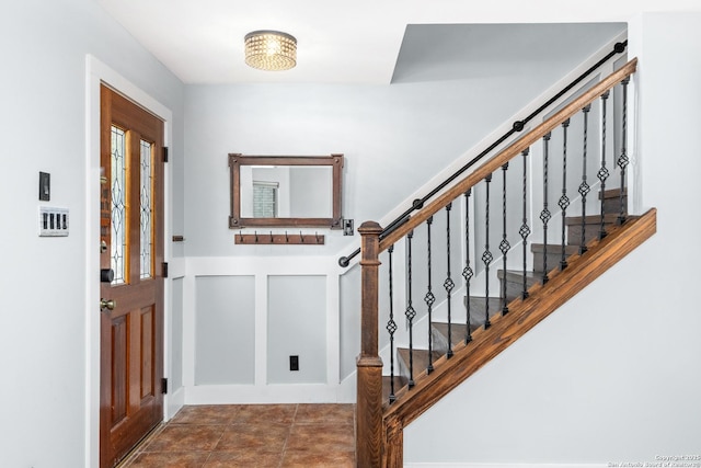 tiled entryway with a decorative wall, wainscoting, and stairway