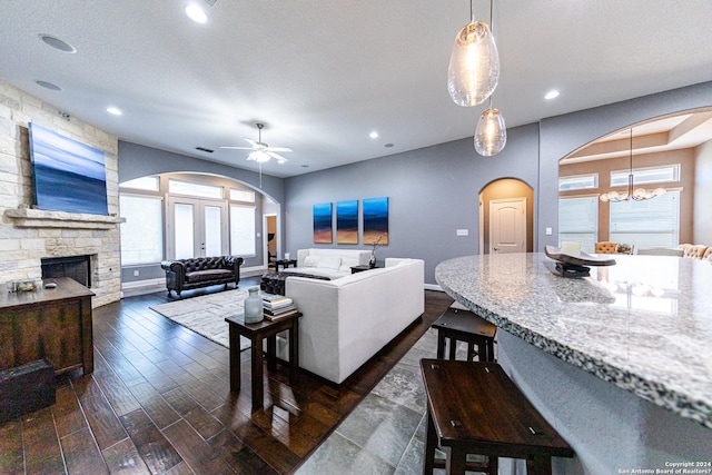 living room with dark wood-type flooring, ceiling fan with notable chandelier, arched walkways, a fireplace, and baseboards