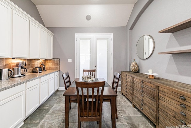 dining area featuring stone finish flooring, french doors, arched walkways, baseboards, and vaulted ceiling