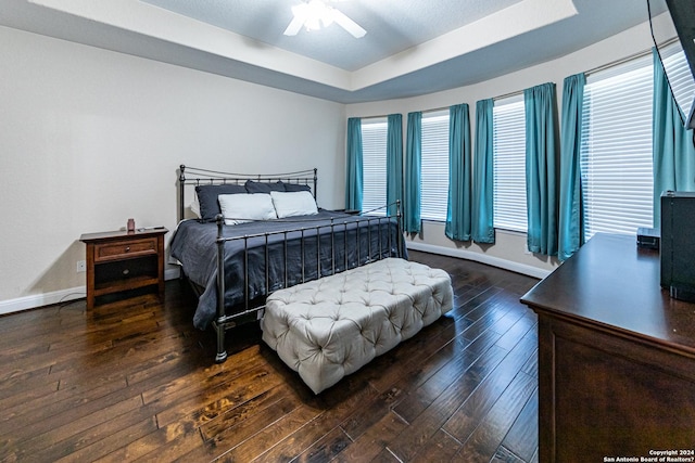 bedroom with a ceiling fan, a raised ceiling, dark wood-style floors, and baseboards