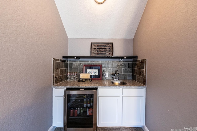 bar featuring a sink, a bar, beverage cooler, and a textured wall