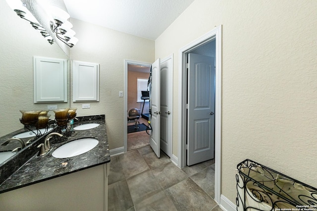 bathroom featuring double vanity, a textured wall, baseboards, and a sink