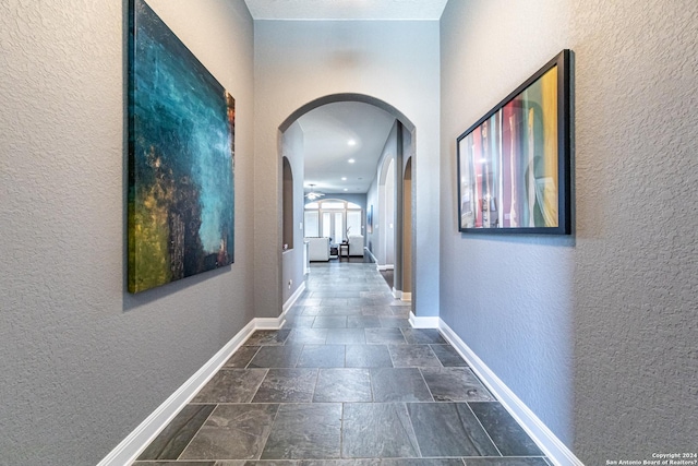 hall with baseboards, arched walkways, and a textured wall