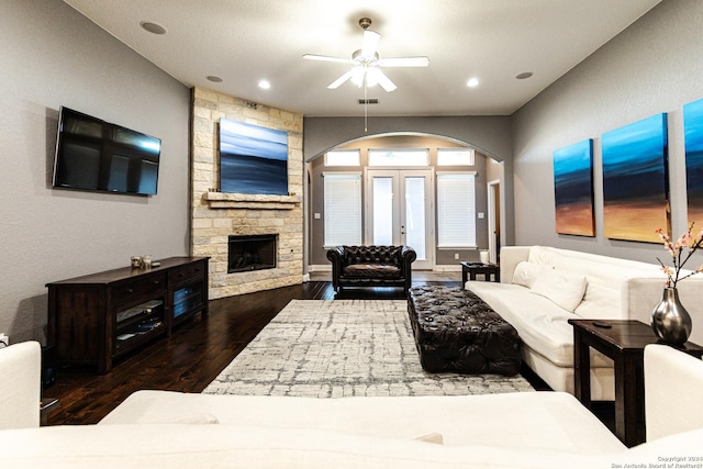 living room with wood finished floors, french doors, arched walkways, a stone fireplace, and ceiling fan