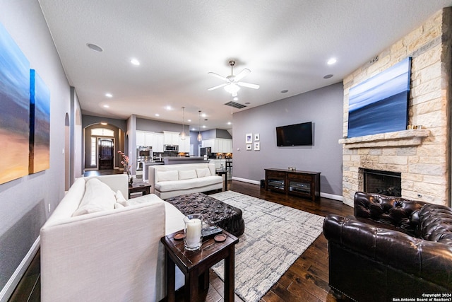 living area with a stone fireplace, dark wood-style floors, arched walkways, and baseboards