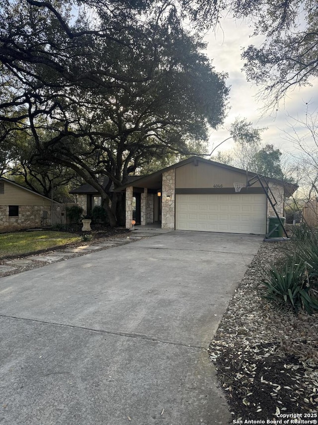 mid-century modern home featuring concrete driveway, a garage, and stone siding