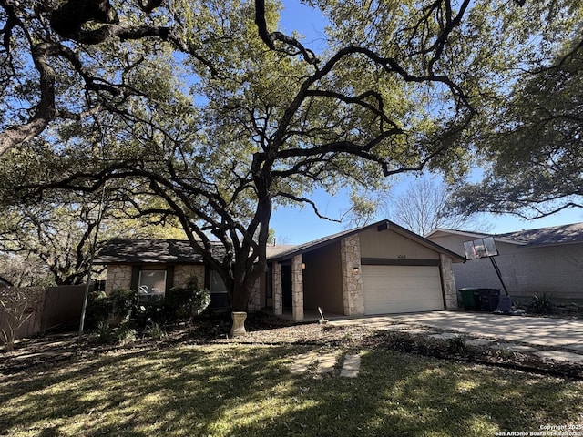 mid-century modern home with an attached garage, fence, stone siding, and driveway