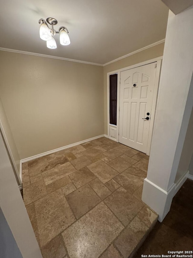 foyer entrance with an inviting chandelier, crown molding, stone tile floors, and baseboards