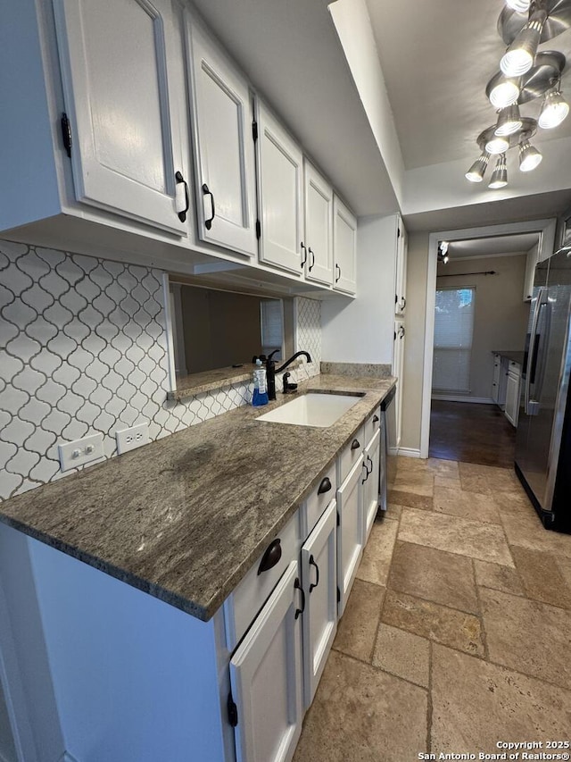 kitchen with tasteful backsplash, stone tile floors, white cabinets, stainless steel appliances, and a sink