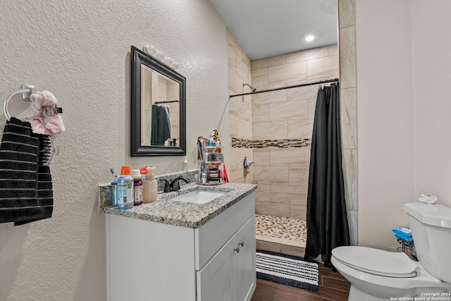 full bath with a tile shower, toilet, a textured wall, and wood finished floors