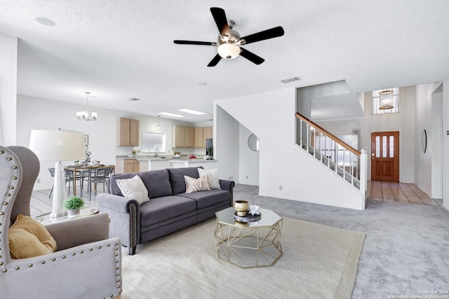 living area featuring visible vents, light carpet, ceiling fan with notable chandelier, a textured ceiling, and stairway