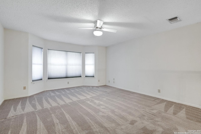 empty room with visible vents, carpet, a ceiling fan, and a textured ceiling