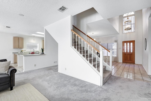 entrance foyer with light tile patterned floors, visible vents, stairs, light colored carpet, and a chandelier