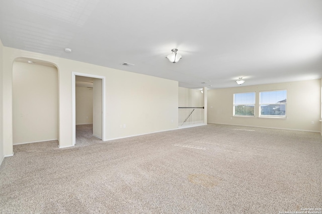 spare room featuring visible vents, arched walkways, light colored carpet, and baseboards