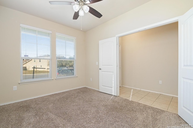 empty room featuring light tile patterned floors, light colored carpet, and a ceiling fan