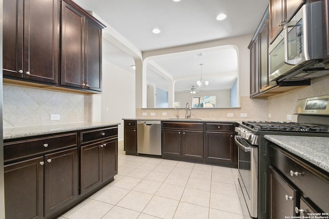 kitchen with dark brown cabinets, decorative backsplash, appliances with stainless steel finishes, light tile patterned flooring, and a sink