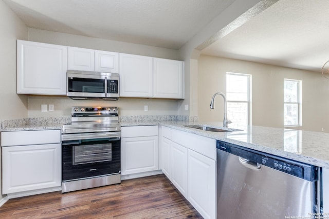 kitchen with a sink, light stone counters, appliances with stainless steel finishes, white cabinets, and dark wood-style flooring