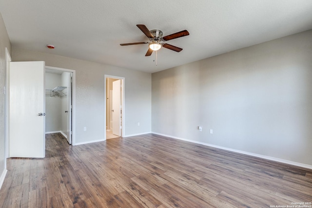 unfurnished bedroom featuring a spacious closet, baseboards, wood finished floors, a closet, and ensuite bath