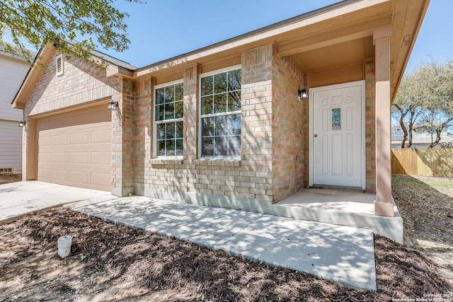 doorway to property with an attached garage, fence, brick siding, and driveway