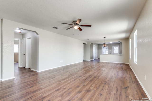 unfurnished living room with visible vents, arched walkways, ceiling fan, and dark wood-style flooring