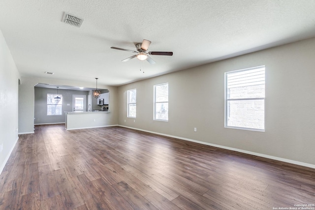 unfurnished living room with a textured ceiling, dark wood-type flooring, visible vents, and ceiling fan