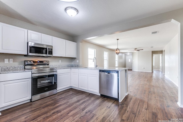 kitchen featuring a sink, appliances with stainless steel finishes, a peninsula, white cabinets, and dark wood-style flooring