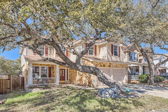 traditional home with stone siding, a porch, fence, concrete driveway, and a garage