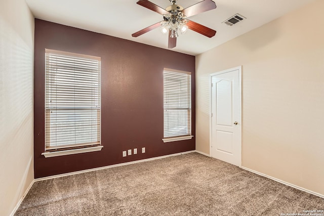 empty room with carpet flooring, a ceiling fan, and visible vents