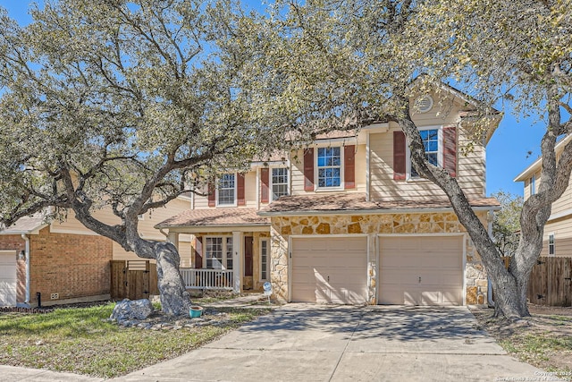 traditional-style home featuring fence, covered porch, concrete driveway, a garage, and stone siding