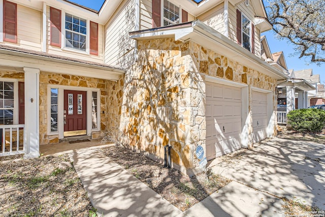 view of exterior entry with stone siding, covered porch, driveway, and a garage