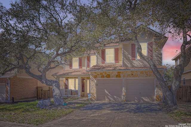 traditional-style home with a garage, stone siding, driveway, and fence