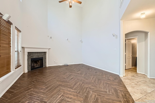 unfurnished living room with arched walkways, a high ceiling, a fireplace, baseboards, and ceiling fan