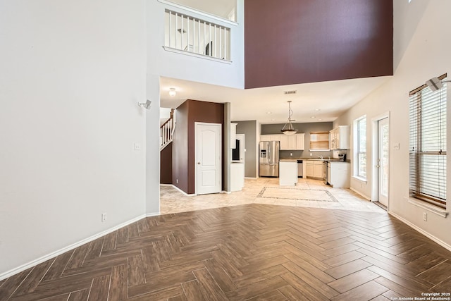 unfurnished living room with stairway, baseboards, visible vents, and a towering ceiling