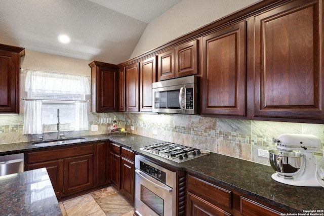 kitchen featuring decorative backsplash, appliances with stainless steel finishes, dark stone counters, and a sink