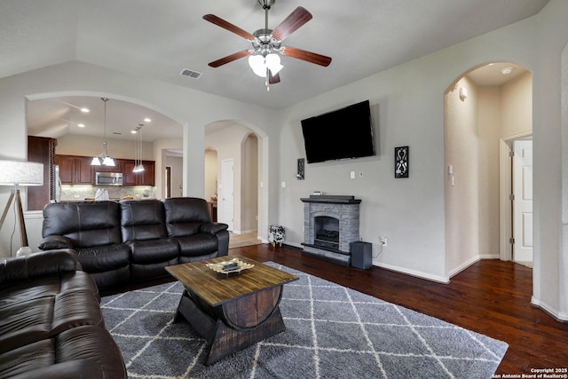 living room featuring visible vents, baseboards, dark wood finished floors, vaulted ceiling, and a fireplace