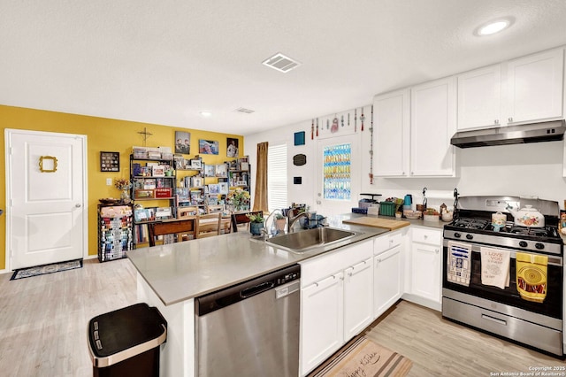 kitchen with a peninsula, a sink, white cabinets, under cabinet range hood, and appliances with stainless steel finishes