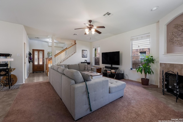 living room featuring ceiling fan, visible vents, light tile patterned flooring, and stairs