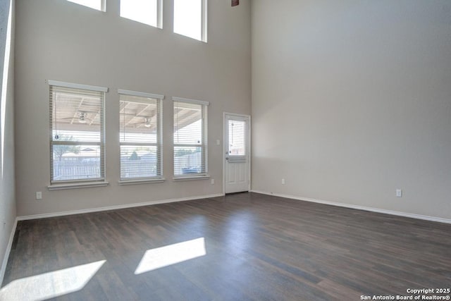 unfurnished living room featuring baseboards, a high ceiling, and dark wood finished floors