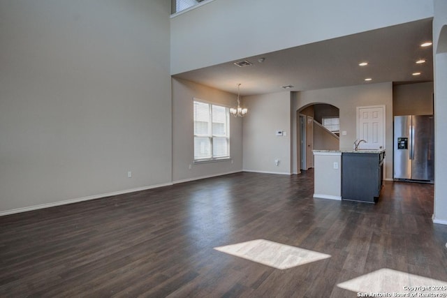 unfurnished living room featuring baseboards, a chandelier, arched walkways, dark wood-style floors, and a sink