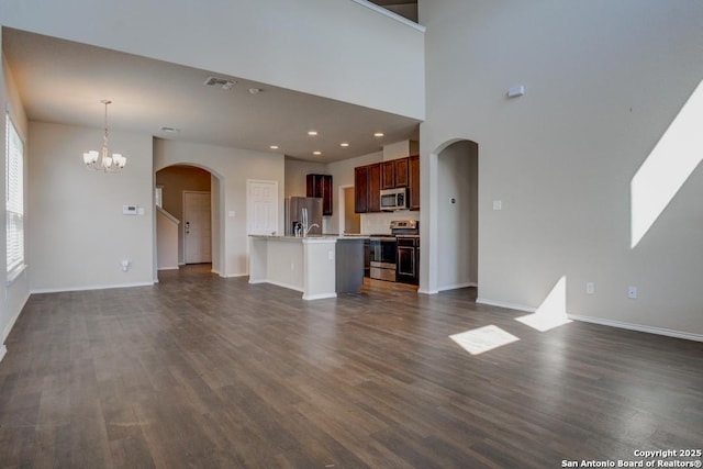 unfurnished living room with visible vents, arched walkways, dark wood-type flooring, and a notable chandelier