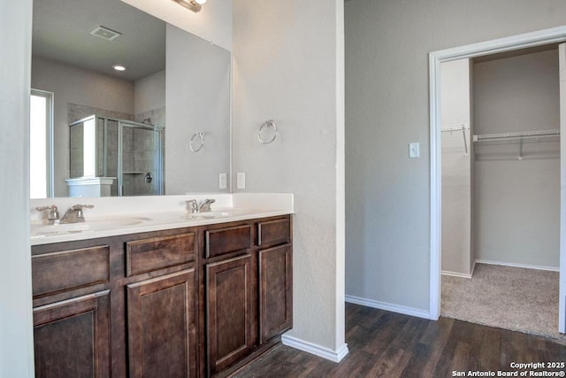 full bath featuring a stall shower, wood finished floors, a walk in closet, and double vanity