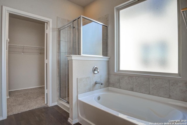 bathroom featuring wood finished floors, a garden tub, a stall shower, and a spacious closet