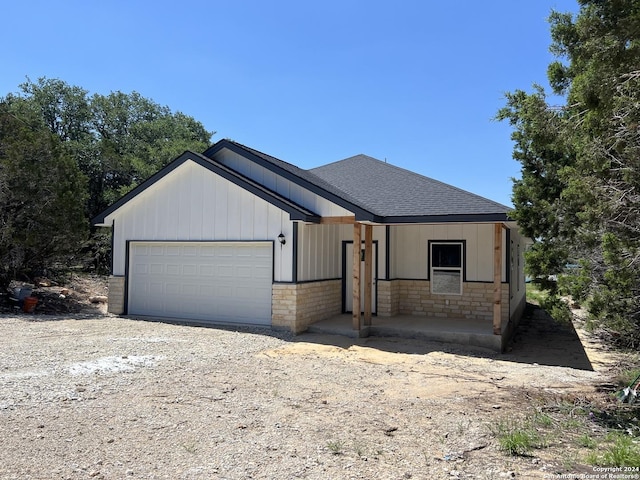 view of front of property with a garage, stone siding, driveway, and roof with shingles