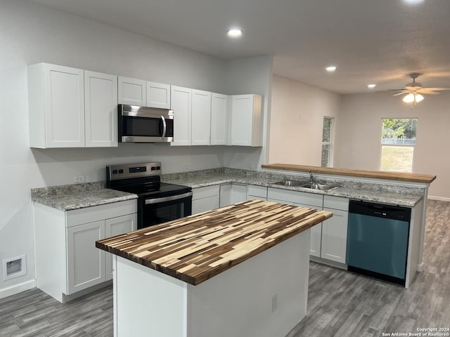 kitchen with butcher block countertops, appliances with stainless steel finishes, a peninsula, white cabinetry, and a sink