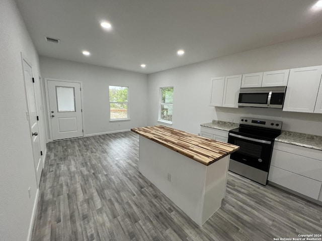 kitchen featuring visible vents, a kitchen island, wood finished floors, stainless steel appliances, and butcher block counters