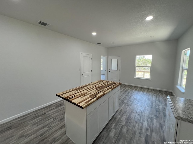 kitchen featuring visible vents, a kitchen island, dark wood finished floors, butcher block countertops, and white cabinetry