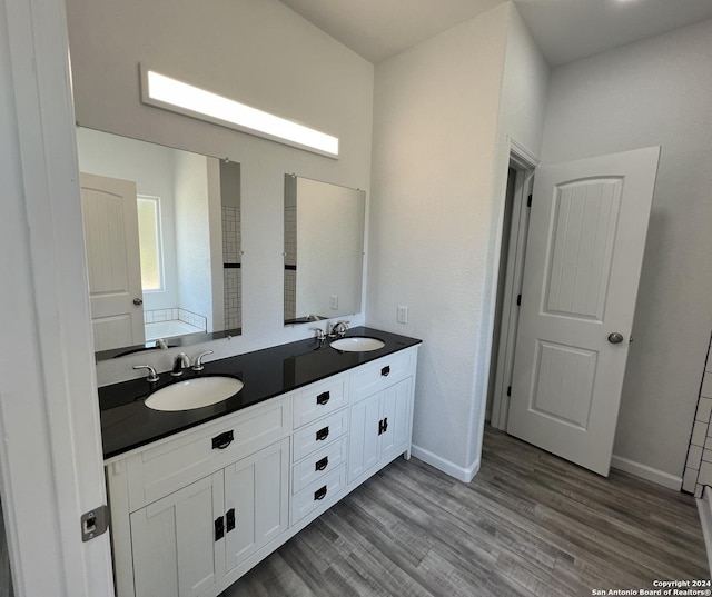 full bathroom featuring a sink, baseboards, wood finished floors, and double vanity